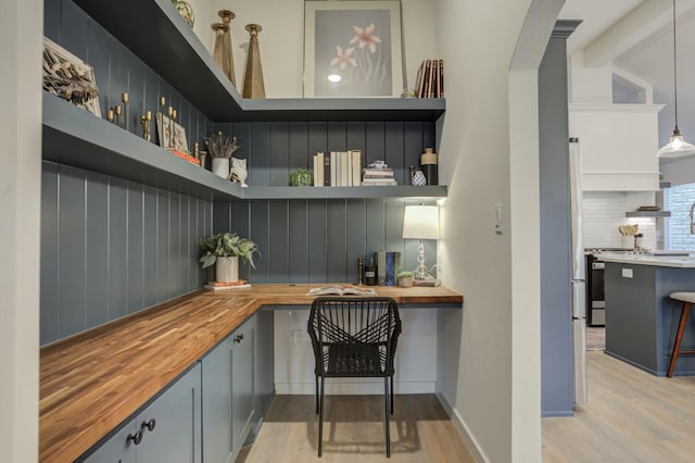 home office with beam ceiling, built in desk, and light hardwood / wood-style flooring