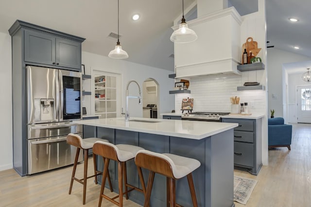 kitchen with hanging light fixtures, an island with sink, sink, and stainless steel fridge