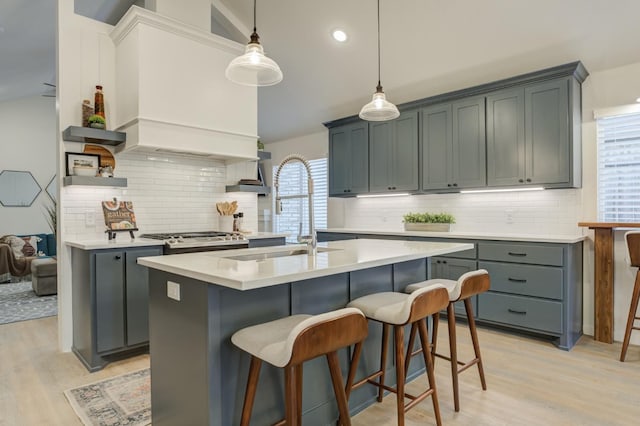 kitchen with pendant lighting, sink, light hardwood / wood-style flooring, a kitchen island with sink, and a kitchen breakfast bar