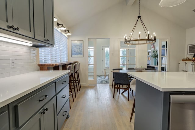 kitchen featuring pendant lighting, gray cabinets, backsplash, high vaulted ceiling, and light hardwood / wood-style floors