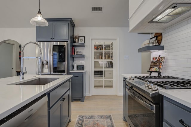 kitchen featuring premium range hood, sink, light hardwood / wood-style flooring, pendant lighting, and stainless steel appliances