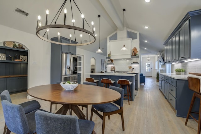 dining area featuring vaulted ceiling with beams, an inviting chandelier, and light hardwood / wood-style floors