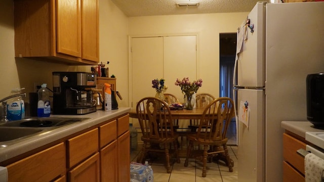 kitchen featuring white refrigerator, light tile patterned flooring, sink, and a textured ceiling