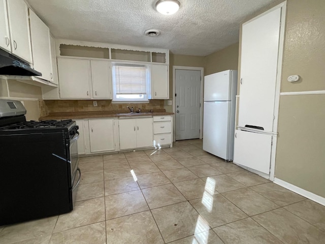 kitchen featuring black gas range oven, sink, light tile patterned floors, white refrigerator, and white cabinets