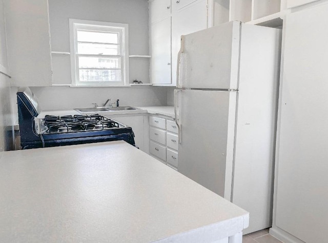 kitchen featuring white refrigerator, white cabinetry, sink, and gas stove