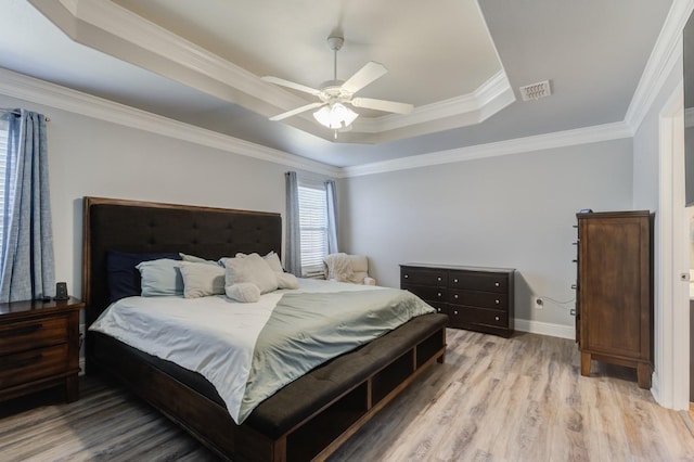 bedroom with ornamental molding, light wood-type flooring, ceiling fan, and a tray ceiling