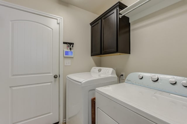 clothes washing area with separate washer and dryer and cabinets