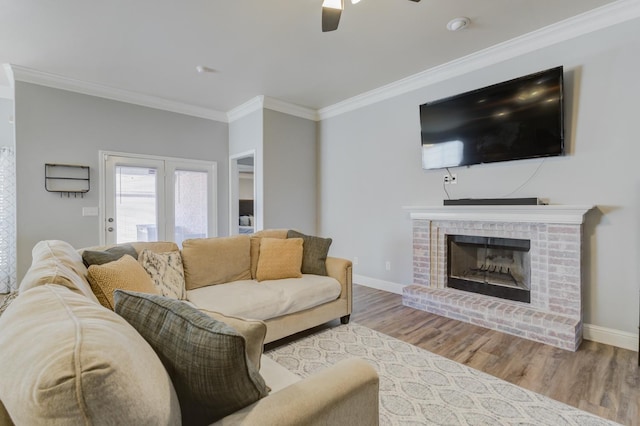 living room featuring ceiling fan, ornamental molding, a fireplace, and light wood-type flooring