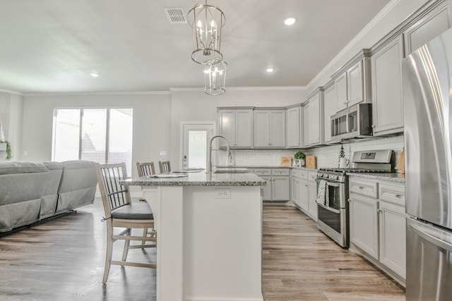 kitchen with a kitchen bar, sink, hanging light fixtures, a center island with sink, and appliances with stainless steel finishes