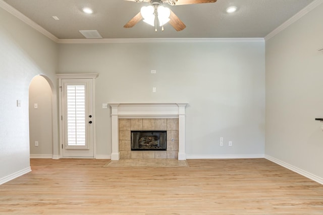 unfurnished living room featuring a tile fireplace, crown molding, ceiling fan, and light hardwood / wood-style flooring