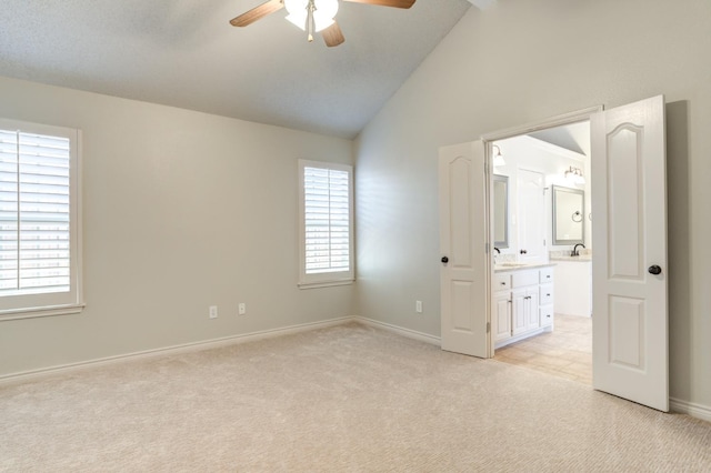 unfurnished bedroom with lofted ceiling, sink, ensuite bath, ceiling fan, and light carpet