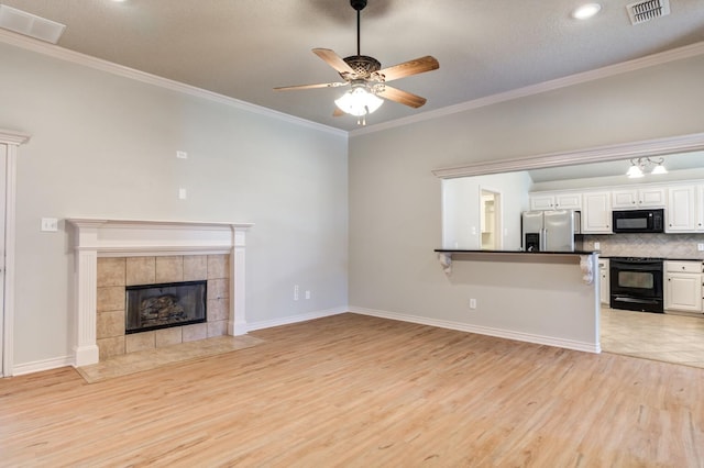 unfurnished living room with a tiled fireplace, ornamental molding, ceiling fan, a textured ceiling, and light hardwood / wood-style flooring