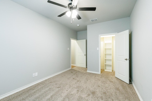 unfurnished bedroom with ceiling fan, light colored carpet, visible vents, baseboards, and a spacious closet