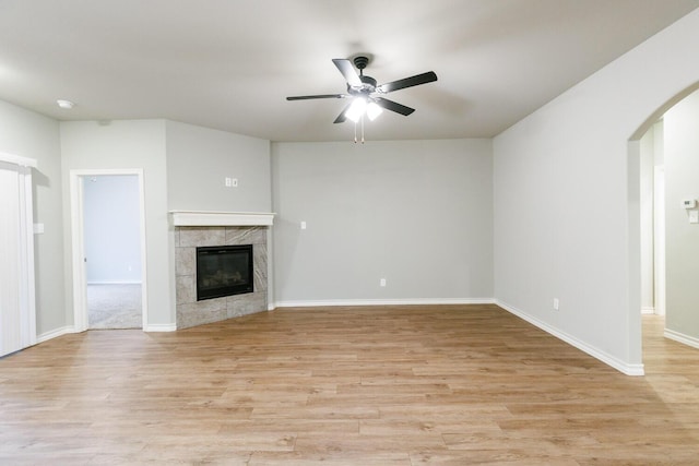 unfurnished living room with light wood-type flooring, ceiling fan, a fireplace, and arched walkways