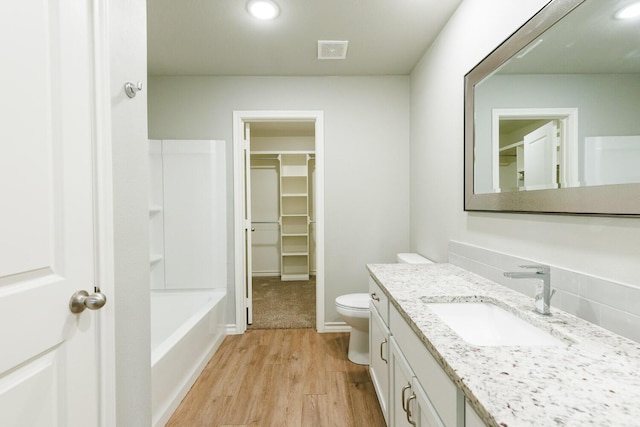 bathroom featuring toilet, wood finished floors, vanity, visible vents, and a tub