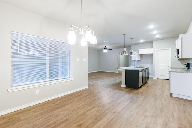 kitchen featuring a center island with sink, hanging light fixtures, light wood-style flooring, open floor plan, and white cabinets