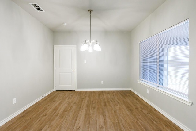 unfurnished room with a chandelier, visible vents, baseboards, and wood finished floors