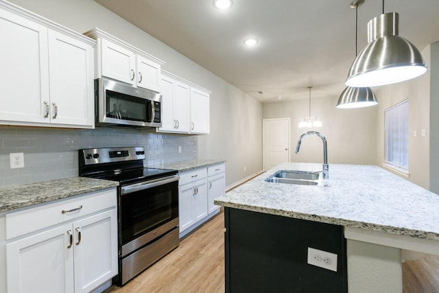 kitchen with stainless steel appliances, tasteful backsplash, light wood-style flooring, a kitchen island with sink, and a sink