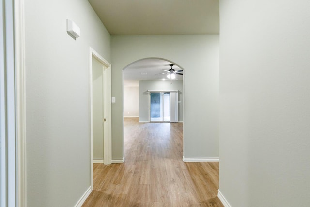 corridor featuring arched walkways, light wood-type flooring, and baseboards