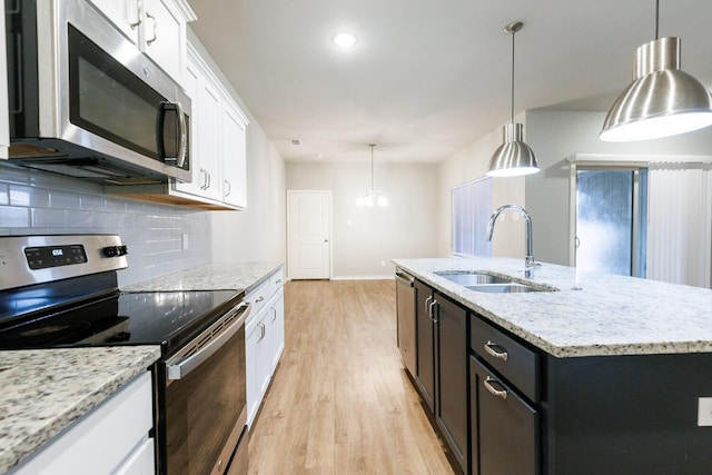 kitchen with light wood finished floors, stainless steel appliances, decorative backsplash, white cabinetry, and a sink