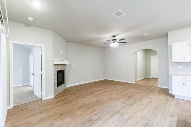 unfurnished living room featuring arched walkways, a fireplace, visible vents, a ceiling fan, and light wood finished floors