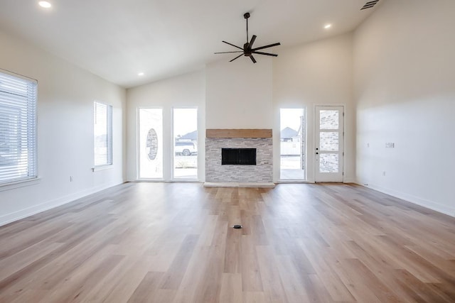 unfurnished living room featuring a stone fireplace, light hardwood / wood-style flooring, high vaulted ceiling, and ceiling fan