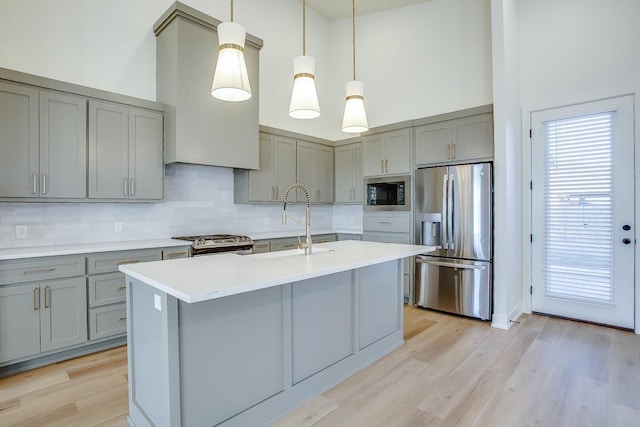 kitchen with a towering ceiling, pendant lighting, sink, gray cabinetry, and stainless steel appliances