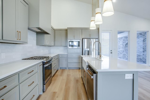 kitchen with custom exhaust hood, hanging light fixtures, a center island with sink, appliances with stainless steel finishes, and gray cabinets