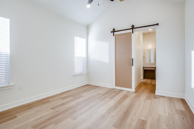 unfurnished bedroom with light hardwood / wood-style flooring, a barn door, ceiling fan, and vaulted ceiling