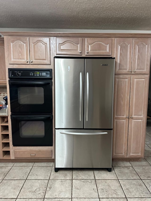 kitchen featuring light brown cabinetry, double oven, stainless steel refrigerator, and a textured ceiling