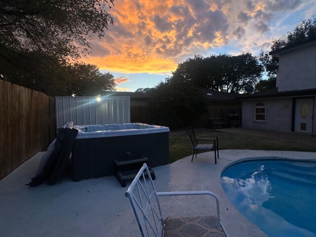 pool at dusk featuring a patio area and a hot tub