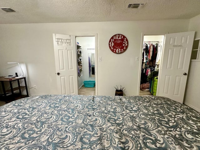 bedroom featuring a walk in closet, ensuite bathroom, a closet, and a textured ceiling