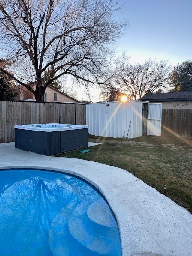 pool at dusk with a yard and a hot tub