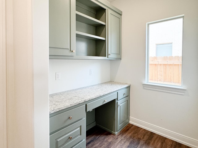 unfurnished office with built in study area, baseboards, and dark wood-type flooring