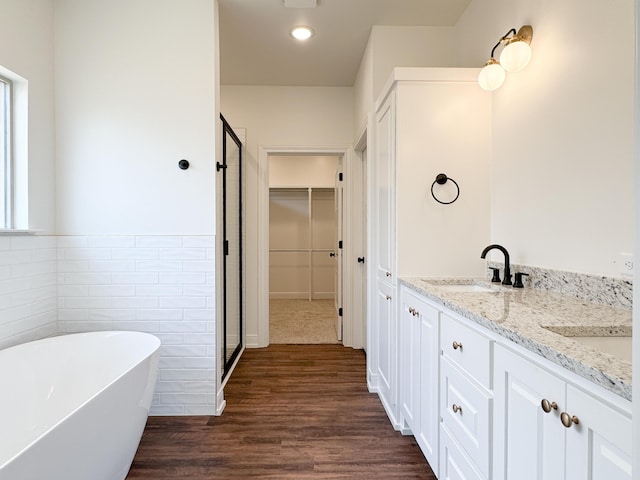 full bathroom featuring a shower stall, wood finished floors, a sink, a walk in closet, and a freestanding tub