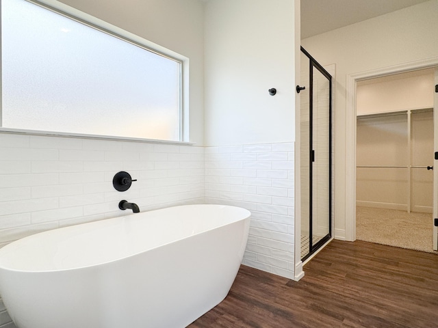 full bath featuring a shower stall, a spacious closet, wood finished floors, tile walls, and a freestanding tub