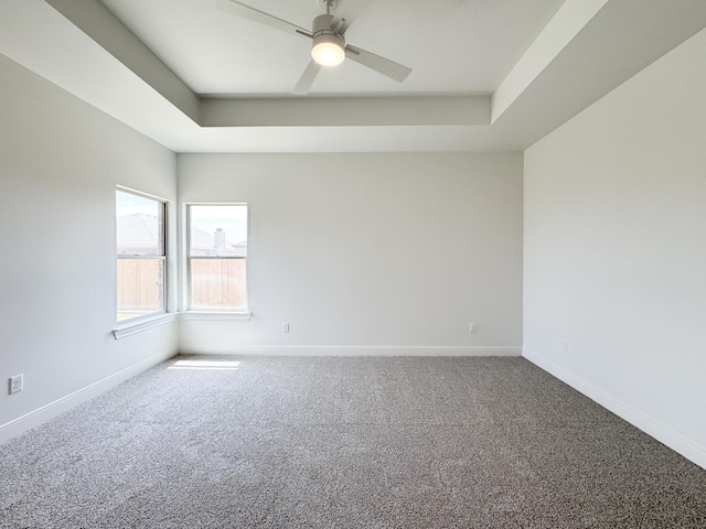 spare room featuring a raised ceiling, carpet floors, a ceiling fan, and baseboards