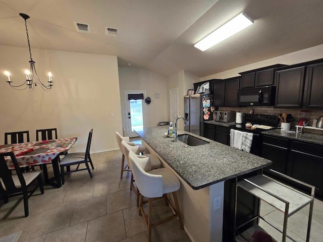 kitchen with sink, dark stone countertops, a breakfast bar area, a kitchen island with sink, and black appliances