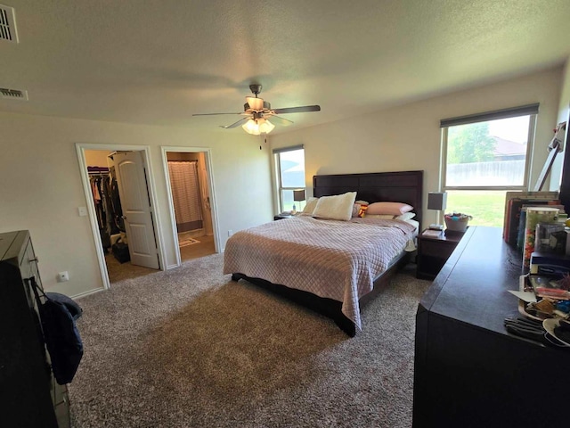 carpeted bedroom featuring ceiling fan, a walk in closet, and a textured ceiling