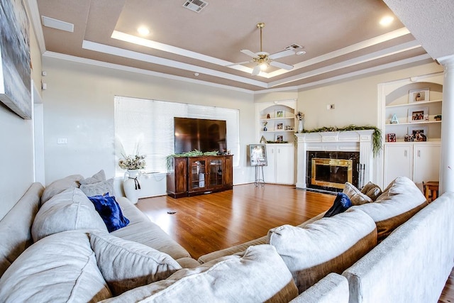 living room with a high end fireplace, a tray ceiling, hardwood / wood-style floors, and built in features