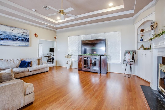 living room with crown molding, wood-type flooring, ceiling fan, and a tray ceiling