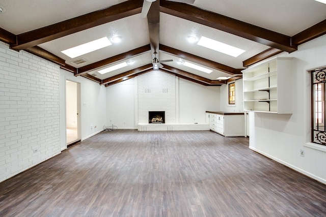 unfurnished living room featuring dark hardwood / wood-style flooring, a fireplace, vaulted ceiling with skylight, and brick wall