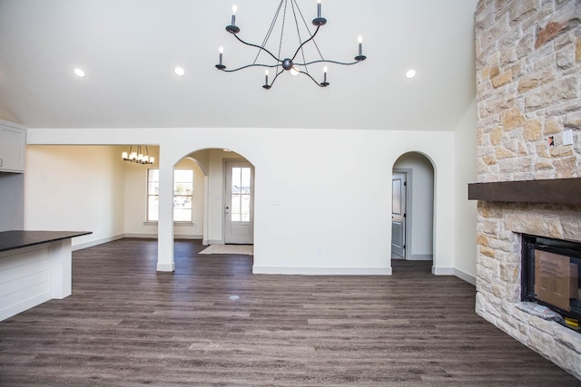 1312 Chaucer Ln, Wolfforth, TX 79382 - unfurnished living room featuring a chandelier, arched walkways, a stone fireplace, dark wood finished floors, and lofted ceiling