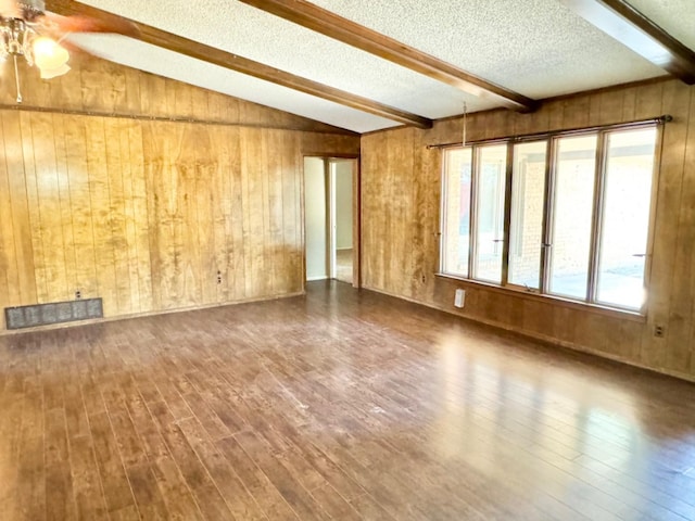 spare room with hardwood / wood-style floors, vaulted ceiling with beams, a textured ceiling, and wood walls