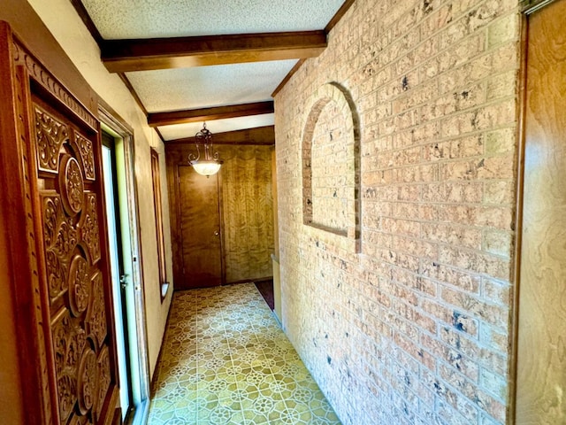 corridor featuring beamed ceiling, brick wall, and a textured ceiling