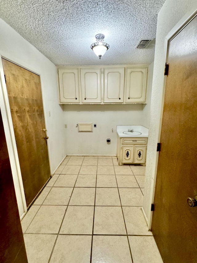 laundry room featuring electric dryer hookup, light tile patterned floors, cabinets, and a textured ceiling