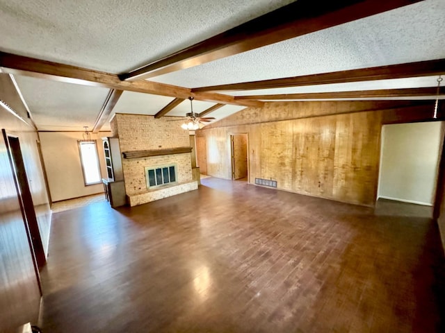 unfurnished living room with ceiling fan, dark hardwood / wood-style floors, a fireplace, lofted ceiling with beams, and a textured ceiling