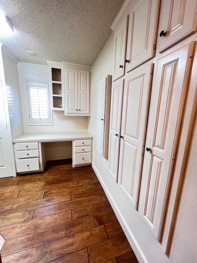 unfurnished office featuring dark hardwood / wood-style flooring, built in desk, and a textured ceiling