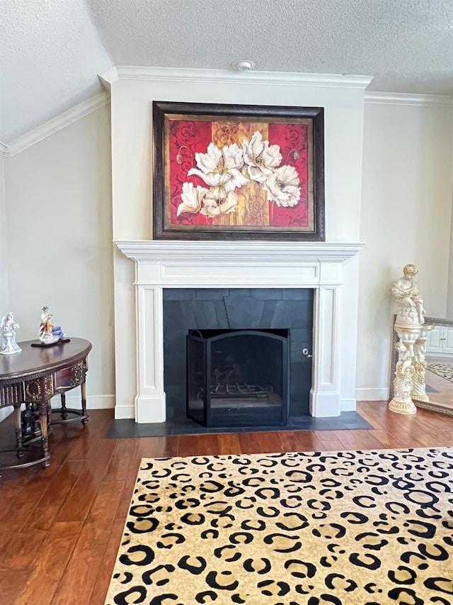 details featuring a tiled fireplace, hardwood / wood-style floors, ornamental molding, and a textured ceiling