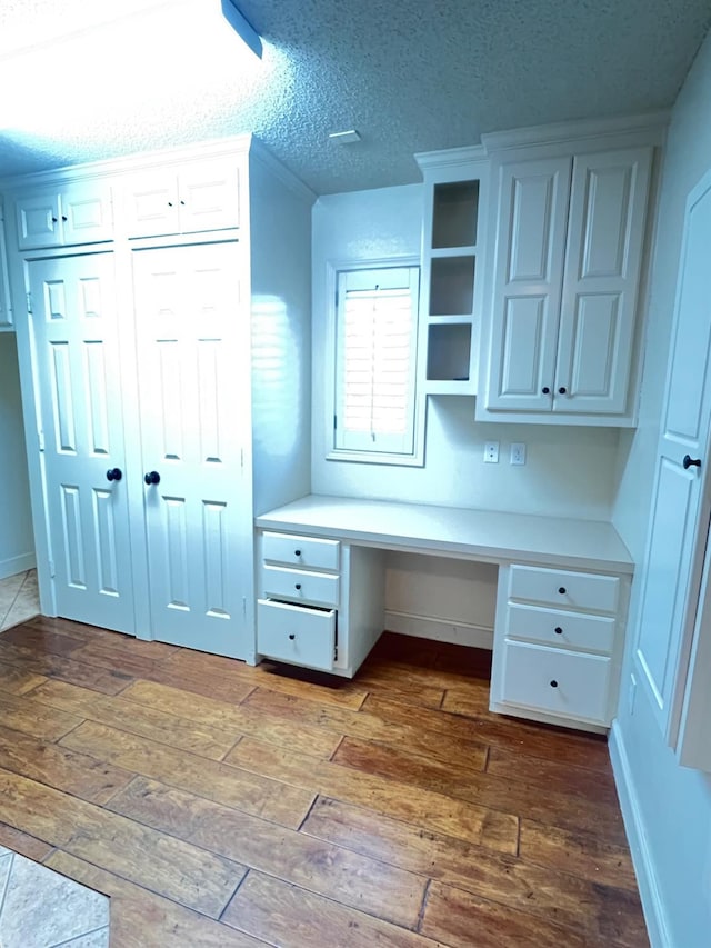 unfurnished office featuring built in desk, hardwood / wood-style floors, and a textured ceiling